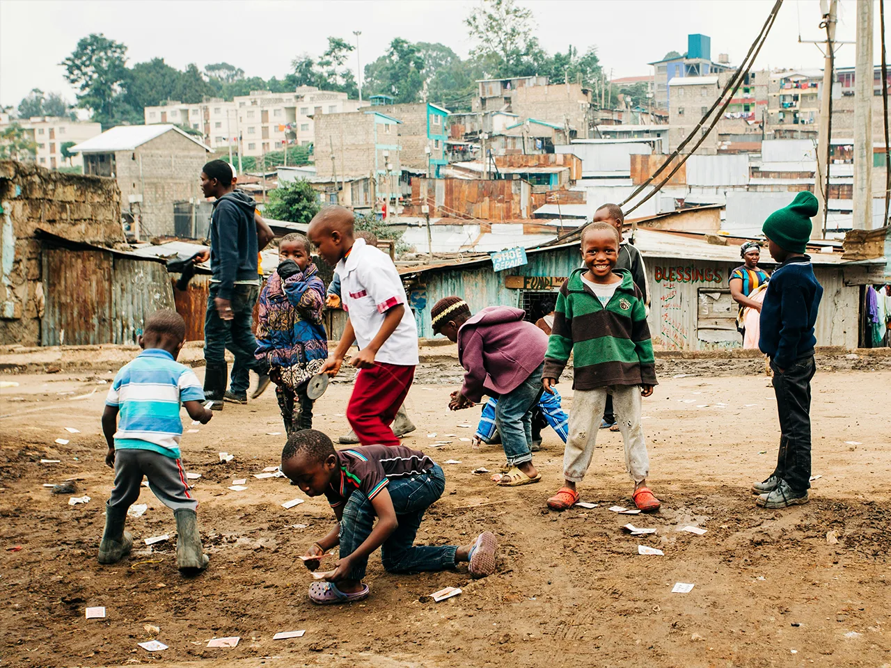 Children play together on the bare ground of an informal settlement.