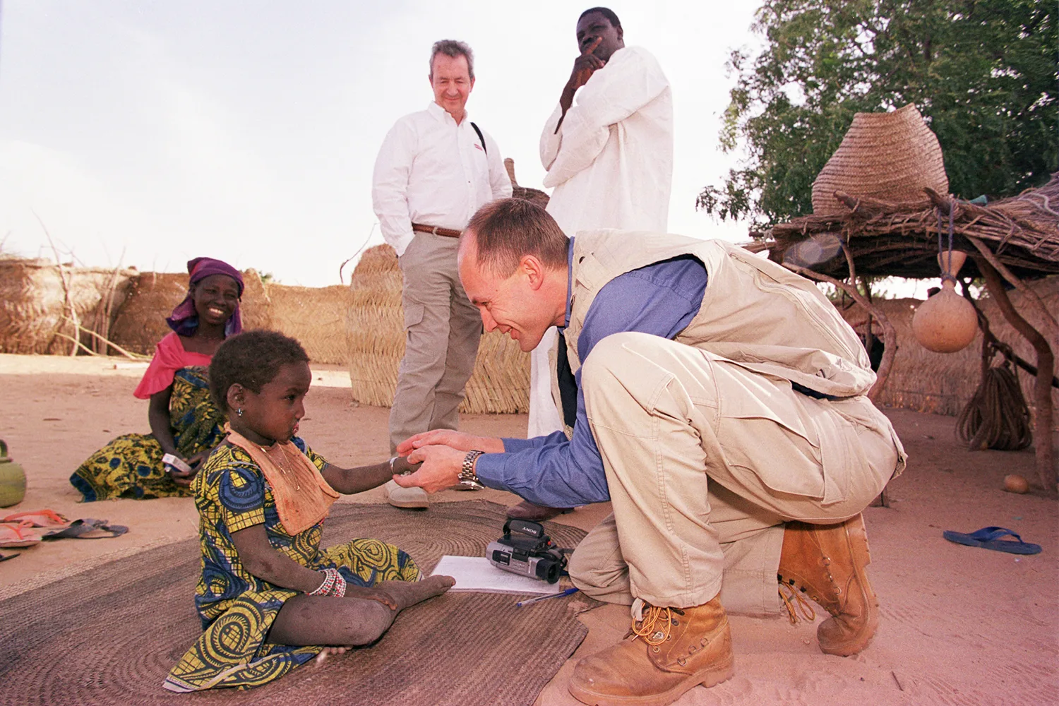 A foundation representative crouches to greet a young girl during a village field visit.